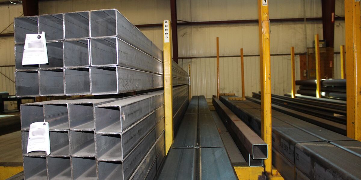 hssinstock Marmon Keystone Stacks of rectangular steel tubing are arranged on racks inside a warehouse. A Marmon/Keystone sign is displayed at the top, highlighting their role as a leading metals distributor. The words "IN STOCK HSS" appear at the bottom of the image.