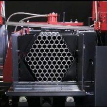 Marmon Keystone A stack of metal pipes arranged in a hexagonal pattern is positioned in a red industrial cutting machine, ready for processing by a leading metals distributor.