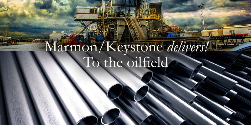 Marmon Keystone Rows of metal pipes are shown in the foreground with an oil drilling rig under a cloudy sky in the background. Text over the image reads, "Marmon/Keystone delivers! Your trusted metals distributor to the oilfield.