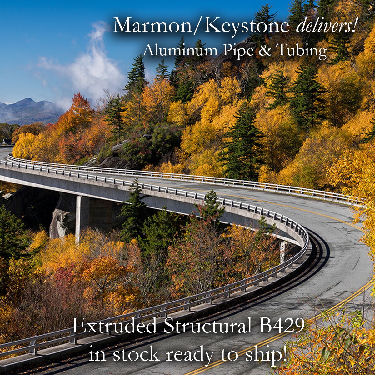 Marmon Keystone A curved highway bridge winds through a forest of autumn trees with vibrant yellow and orange foliage. Text promotes Marmon/Keystone aluminum pipe and tubing, stating Extruded Structural B429 is in stock and ready to ship.