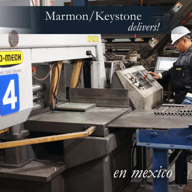 Marmon Keystone A worker operates industrial machinery in a factory setting by Marmon/Keystone. Metal tubes and equipment are visible, with signs in English and Spanish. Text on the image reads: "Marmon/Keystone delivers! en mexico.